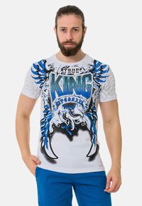 Weißes T-Shirt mit auffälligem blauem und schwarzem Grafikdesign sowie dem Text "ECHTER KÖNIG." Kurze Ärmel und Rundhalsausschnitt, mit einer figurbetonten Passform.
