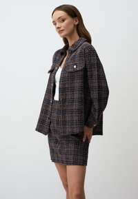 Veste en tweed tissée bleu marine, orange et blanche avec col, deux poches avant et fermeture à bouton. Associée à une mini-jupe en tweed assortie.