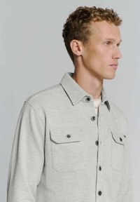 Lichtgrijze, knoopsluiting overhemd met een kraag, twee borstzakken en zwarte knoopdetails; gemaakt van een gestructureerd materiaal, casual pasvorm.