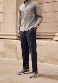 Grijze button-up shirt met een borstzak, gecombineerd met marineblauwe pinstripe broek en grijze sneakers, met een textuurafwerking en ontspannen pasvorm.