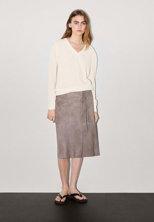 V-neck cream sweater, grey suede wrap skirt with tie detail, and black flip-flops, creating a casual outfit. Smooth textures and muted colors.