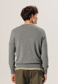 Grauer Pullover aus weichem Strickmaterial mit Rundhalsausschnitt, langen Ärmeln und gerippten Bündchen sowie Saum. Das Design ist schlicht und klassisch.