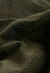 Material de tricot moale, de o nuanță verde închis, cu o suprafață texturată, care prezintă pliuri și curbe delicate, subliniind căldura și flexibilitatea sa.