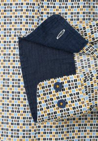 Hemd mit Kragen in einem blauen, schwarzen und braunen geometrischen Muster, mit dunkelblauen Fischgrät-Manschetten und Knöpfen. Strukturierte Stoffdetails sind sichtbar.