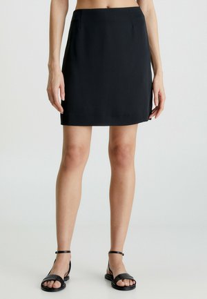 Zwarte minirok met een gladde textuur, rechte snit, zijzakken en een nette zoom, gecombineerd met zwarte platte sandalen.