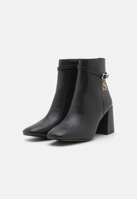 Bottes noires de cheville en cuir lisse, avec un bout pointu, un talon carré et un accent métallique décoratif sur le côté.