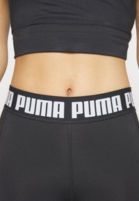 Black athletic leggings featuring a wide waistband with "PUMA" in large white letters. Smooth texture and close-fitting design.