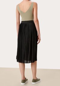 Olivgrön ribbad bodysuit med V-rygg, i kombination med en svart plisserad midikjol och gröna sneakers. Lätt och smidig textur, figurnära liv och elastisk midja.