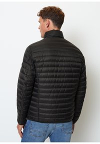Chaqueta de plumas negra aislante con diseño de acolchado horizontal, cuello alto y puños elásticos, combinada con jeans de color azul claro.