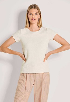 Kurzärmeliges, strukturiertes cremefarbenes Oberteil mit rundem Ausschnitt, kombiniert mit hellrosa Hosen mit Nadelstreifen. Auffällige Details sind das dezente Stoffmuster.