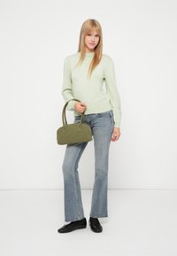 Gaiši zaļš adīts džemperis ar pūkainām piedurknēm, apvienots ar izbalējušiem zilajiem platām biksēm. Tur rokā mazu olīvu zaļu somiņu. Melni dzīvokļi apavi.