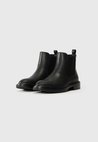 Botas Chelsea de cuero negro con paneles laterales elásticos, punta redonda y tacón bajo apilado. Cuenta con lengüetas para facilitar el uso.