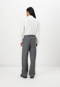 Grey plaid wide-leg pants with an elastic waistband, paired with a white collared shirt, viewed from the back against a white background.