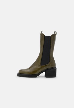 Grüner Lederknöchelstiefel mittlerer Höhe mit schwarzen elastischen Seitenpartien, Zuglaschen und einem klobigen schwarzen Blockabsatz.