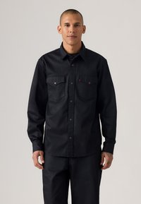 Black denim shirt with long sleeves, two chest pockets, button closure, and a plain texture. Worn with matching dark pants.