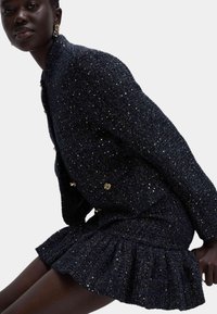 Granatowy zestaw marynarki i spódnicy z tweedu z metalicznymi akcentami, teksturowana tkanina, luźny krój i falbaniasty dół spódnicy. Guziki z motywem kwiatowym.