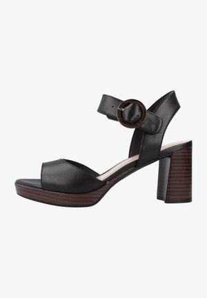 Sandalias de tacón de cuero negro con puntera abierta, correa ancha y correa ajustable en el tobillo con hebilla redonda, sobre un tacón de bloque de madera.