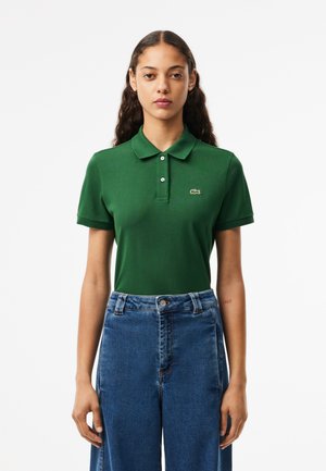 Polo verde con colletto, maniche corte e un piccolo logo ricamato. Abbinato a jeans di denim blu a vita alta.