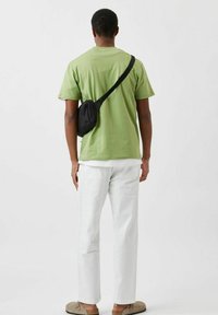 Sort sling taske båret over en løs pasformet lysegrøn t-shirt, parret med hvide straight-leg bukser og beige slip-on sko.