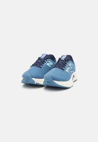 Scarpe da ginnastica blu con upper testurizzato, dotate di una suola intermedia bianca e un prominente logo "N" sul lato. I lacci sono di colore blu scuro.