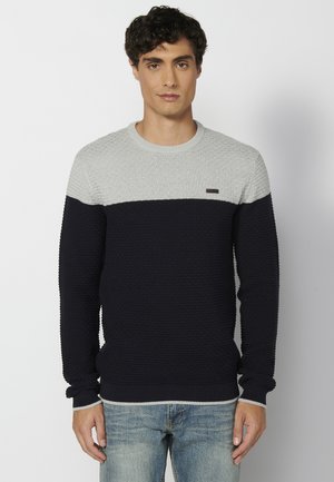 Gebreide trui met een grijze bovenhelft en een donkerblauwe onderhelft, een gestructureerd patroon, geribbelde manchetten en een klein logo op de borst.