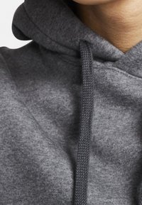 Felpa grigia con cappuccio realizzata in tessuto strutturato, con coulisse visibili e collo aderente, che presenta un design morbido e casual.