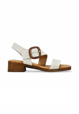 Sanda blanca de cuero con tiras cruzadas y una hebilla de madera redonda, con un tacón bajo y una plantilla suave de color marrón.