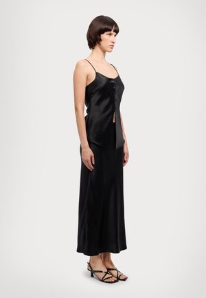 Sort satin top med tynde stropper, med knaplukning og asymmetrisk kant, parret med en matchende lang nederdel og stiletter.