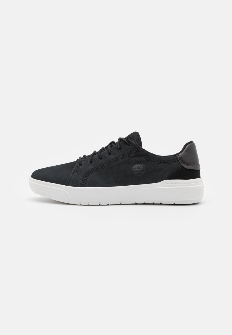 SvartMocka sneakers med vit gummisula, med rund tå, plana snören och en logotypdetalj på sidan. Klassisk atletisk design.