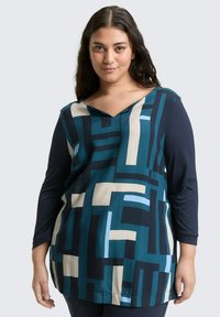Langearmige top met een geometrisch patroon in blauw, teal en crème. V-hals ontwerp met contrasterende mouwen en een zachte textuur.