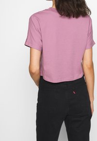 Avklippt t-shirt med kort ärm i ljusrosa, tillverkad av mjukt tyg; i kombination med svarta denimjeans med hög midja och bakfickor.