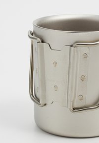 Mug de camping en acier inoxydable avec une forme courbée. Présente une bande en métal texturé gris et une poignée en métal robuste avec des rivets visibles.