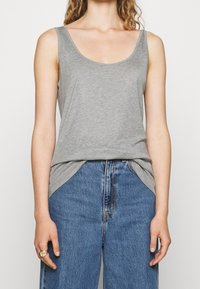 Grijze mouwloze top van zachte stof, met een ronde halslijn en een losse pasvorm, gecombineerd met high-waisted blauwe spijkerbroeken.