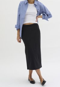 Czarna midi spódnica o gładkiej teksturze połączona z białym prążkowanym topem na ramiączkach oraz niebieską i białą w paski koszulą z podwiniętymi rękawami. Czarne baleriny.