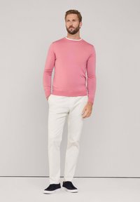 Suéter de punto rosa claro con un cuello redondo, combinado con pantalones blancos ajustados y zapatillas de deporte azul marino, todo sobre un fondo minimalista.