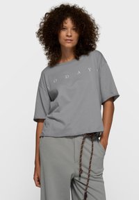 T-shirt gris court à manches courtes, avec le mot "AUJOURD'HUI" imprimé en blanc sur le devant. Tissu doux, coupe décontractée.