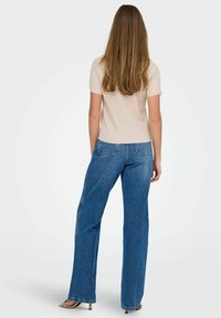 Beżowa, prążkowana bluzka z krótkim rękawem w zestawieniu z niebieskimi dżinsami z wysokim stanem. Spodnie mają luźny krój, kieszenie i prostą nogawkę.