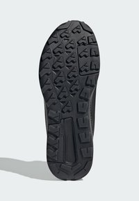 Čierna podrážka topánky s textúrovanou gumou, ktorá má viacero smerových drážok a centrálnu drážku pre trakciu. Odolný dizajn pre grip.
