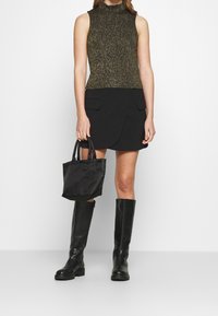 Top sin mangas de punto metálico dorado; falda negra cruzada con bolsillos; bolso negro pequeño; botas de cuero negro hasta la rodilla; textura suave.