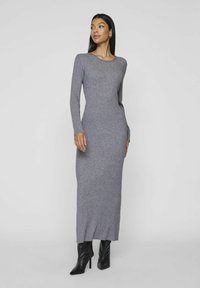 Gray ribbed knit maxi dress with long sleeves and a round neckline. The dress features a fitted silhouette and side slits, paired with black heels.