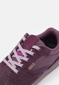 Scarpa sportiva viola con un mix di suede e tessuto, superficie testurizzata, lacci bianchi e un'etichetta con logo sul lato.