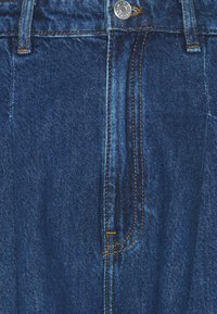Close-up of blue denim jeans front with metal button, orange stitching, and belt loops.