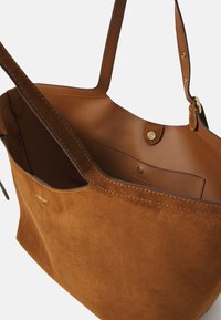 Borsa a tracolla in suede marrone vista dall'alto, dotata di due manici e di un interno aperto con una tasca e chiusura a bottone.