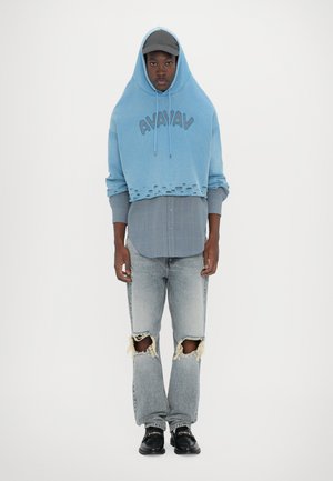 Light blue cropped hoodie with a drawstring hood, layered over a gray plaid shirt. Worn with distressed light wash jeans and black shoes.