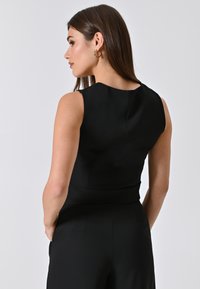 Top senza maniche nero con una texture liscia, caratterizzato da un collo alto e una silhouette aderente, mostrato da un angolo laterale.