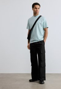 Μέντα πράσινο κοντομάνικο μπλουζάκι με μαύρο λογότυπο στο γιακά, σε συνδυασμό με μαύρο παντελόνι cargo με πλαϊνές τσέπες και φαρδιά μπατζάκια.