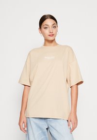 Beige oversized t-shirt lavet af blødt stof, med rund halsudskæring og korte ærmer. Fronten prydes af hvid tekst "PACIFIC COAST."