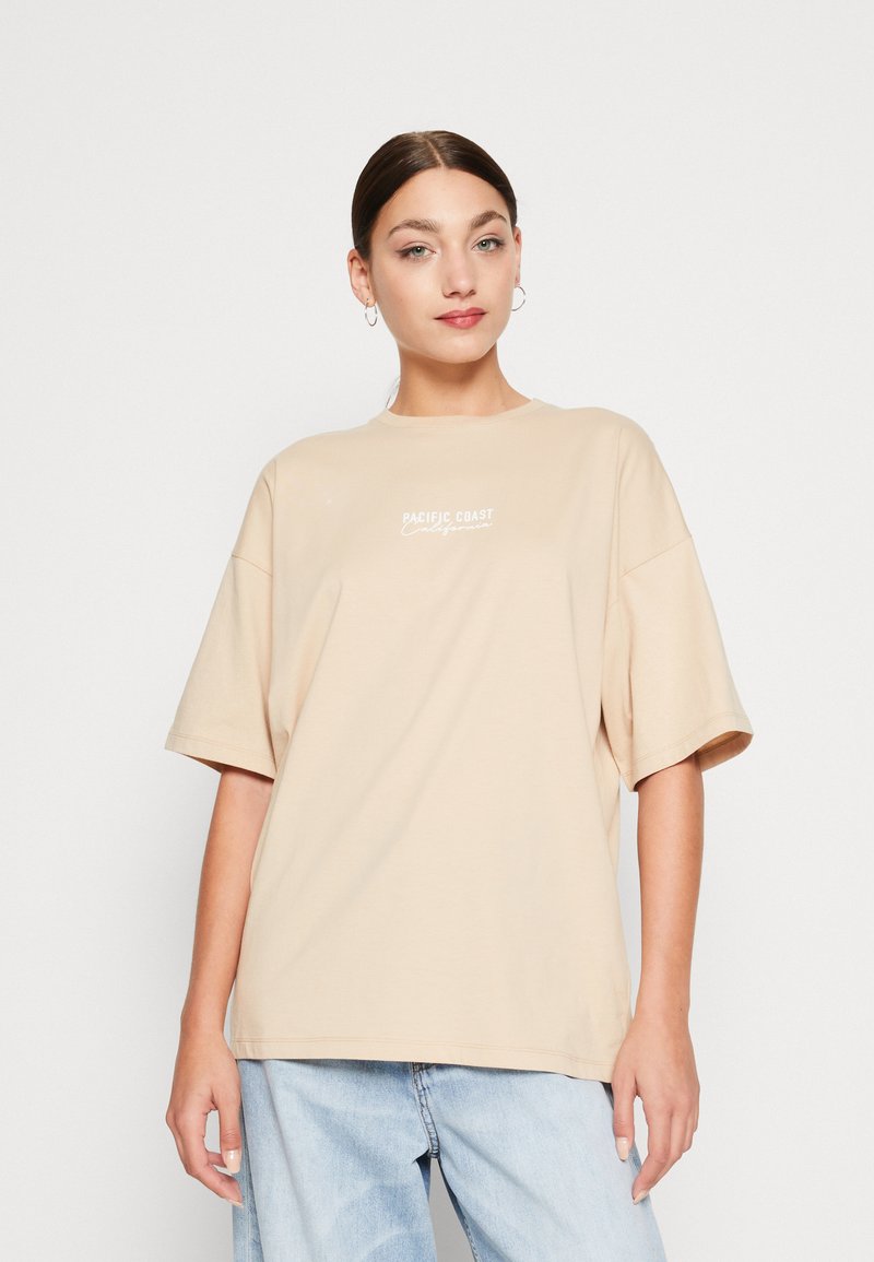 Beige oversized t-shirt lavet af blødt stof, med rund halsudskæring og korte ærmer. Fronten prydes af hvid tekst "PACIFIC COAST."
