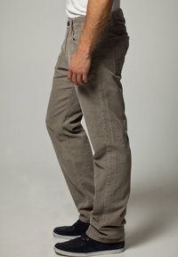 Jasnoszare spodnie sztruksowe o prostym kroju, z bocznymi kieszeniami i zapięciem na guziki, w zestawieniu z ciemnoniebieskimi butami z płótna.