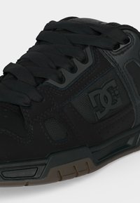 Μαύρο παπούτσι skateboard της μάρκας DC με υφή στην πλαϊνή επιφάνεια, δέσιμο με κορδόνια και λαστιχένια σόλα με ανάγλυφο σχέδιο.